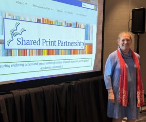 Miranda Bennett standing next to a large screen displaying the landing page of the Shared Print Partnership website